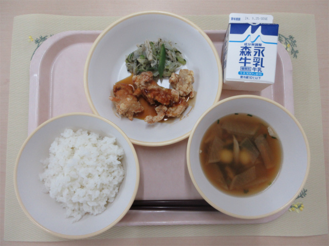 ピンクのトレーに給食が右上から反時計回りで牛乳、磯香和え、鶏肉のかりん揚げ、ごはん、月見汁と並べられている写真