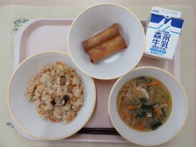 ピンクのトレーに給食が右上から反時計回りで牛乳、春巻き、中華おこわ、切り干し大根のピリ辛スープと並べられている写真