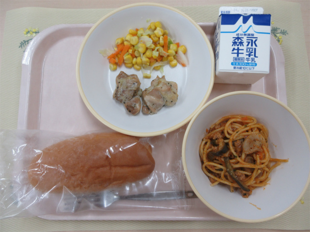 ピンクのトレーに給食が右上から反時計回りで牛乳、コーンソテー、鶏肉のハーブ焼き、コッペパン、なすのミートソーススパゲッティと並べられている写真