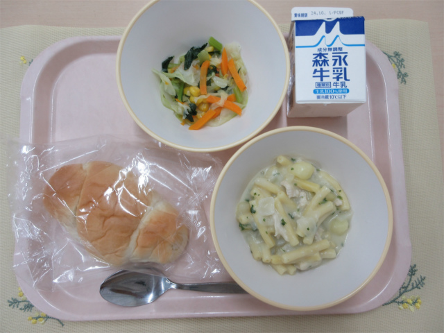 ピンクのトレーに給食が右上から反時計回りで牛乳、野菜ソテー、ロールパン、マカロニのクリーム煮と並べられている写真