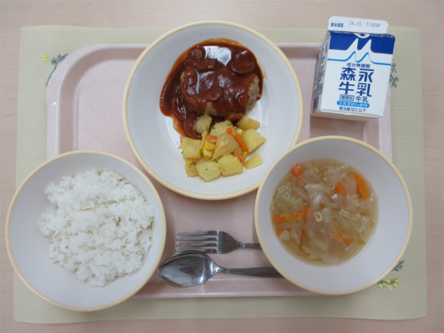 ピンクのトレーに給食が右上から反時計回りで牛乳、デミグラスハンバーグ、じゃがいものソテー、ごはん、ABCスープと並べられている写真