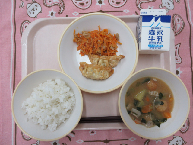 ピンクのトレーに給食が右上から反時計回りで牛乳、にんじんしりしり 、揚げ餃子、ごはん 、さつま汁と並べられている写真