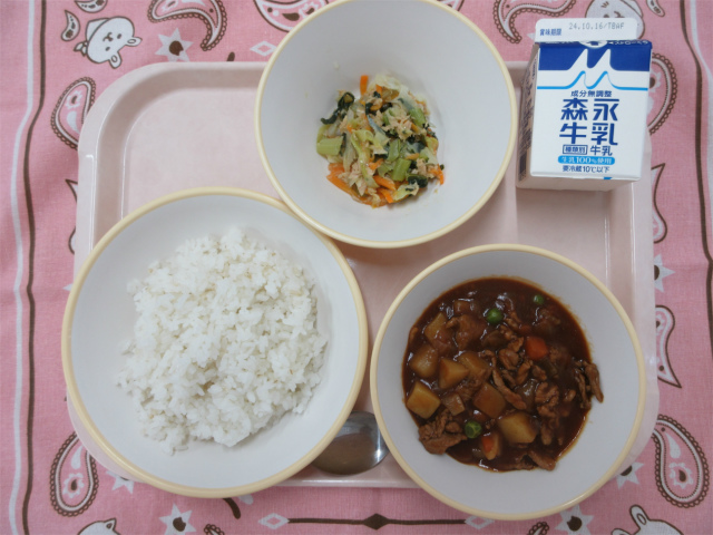 ピンクのトレーに給食が右上から反時計回りで牛乳、野菜のツナ炒め 、麦入りごはん、ハヤシライスと並べられている写真