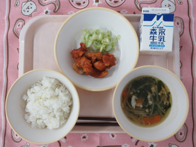 ピンクのトレーに給食が右上から反時計回りで牛乳、千切りキャベツ 、ヤンニョムチキン、ごはん 、五目中華スープと並べられている写真