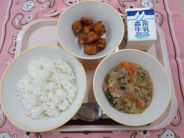ピンクのトレーに給食が右上から反時計回りで牛乳、あげいも、ごはん、中華丼のあんと並 べられている写真