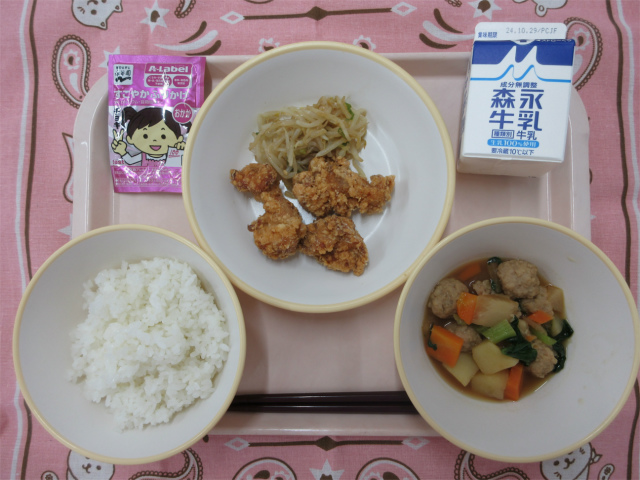 ピンクのトレーに給食が右上から反時計回りで牛乳、もやしの中華和え、鶏の竜田揚げ、おかかふりかけ、ごはん、根菜と肉だんごの煮物と並べられている写真