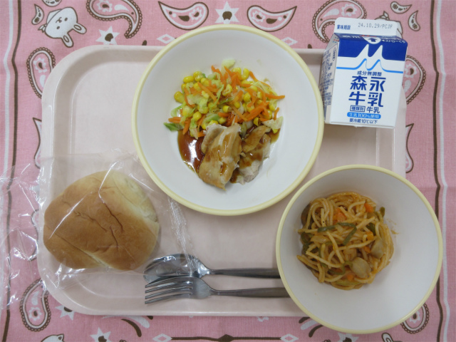 ピンクのトレーに給食が右上から反時計回りで牛乳、コーンソテー、照り焼きチキン、ロールパン、スパゲティナポリタンと並べられている写真