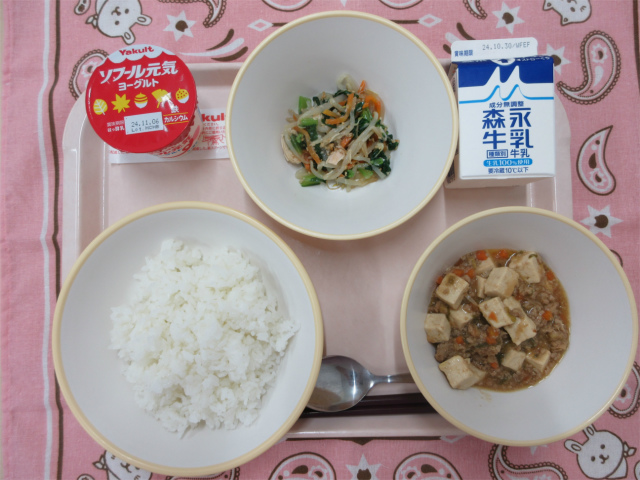 ピンクのトレーに給食が右上から反時計回りで牛乳、鶏肉と野菜のナムル、ヨーグルト、ごはん、麻婆豆腐丼の具と並べられている写真