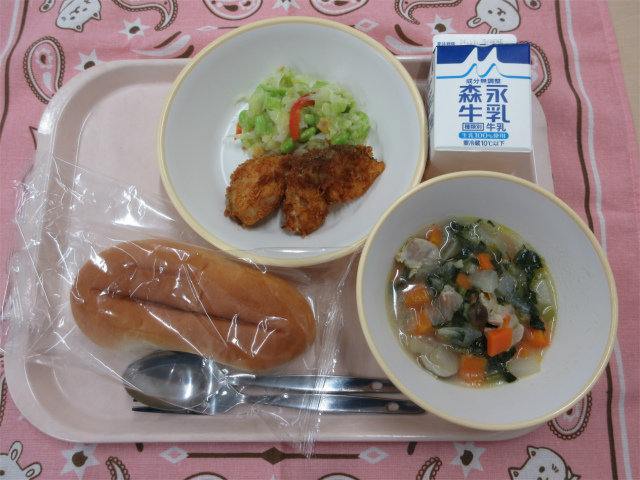 ピンクのトレーに給食が右上から反時計回りで牛乳、コーンドレッシングサラダ、白身魚のフライ、ソフトフランスパン、チキンポトフと並べられている写真