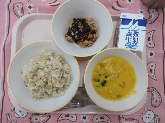 ピンクのトレーに給食が右上から反時計回りで牛乳、黒ゴマあまだれスパイシーチキン、ガーリックライス、かぼちゃのクリームスープと並べられている写真