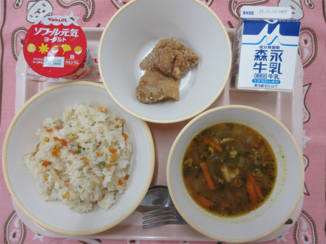 ピンクのトレーに給食が右上から反時計回りで牛乳、鶏肉のから揚げ、ヨーグルト、ベジピラフ、青パパイヤのカレースープと並べられている写真