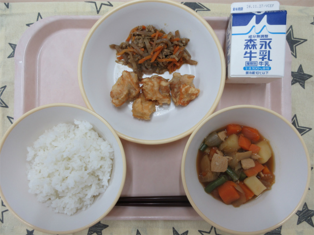 ピンクのトレーに給食が右上から反時計回りで牛乳、きんぴら、鶏天、ごはん、野菜の旨煮と並べられている写真