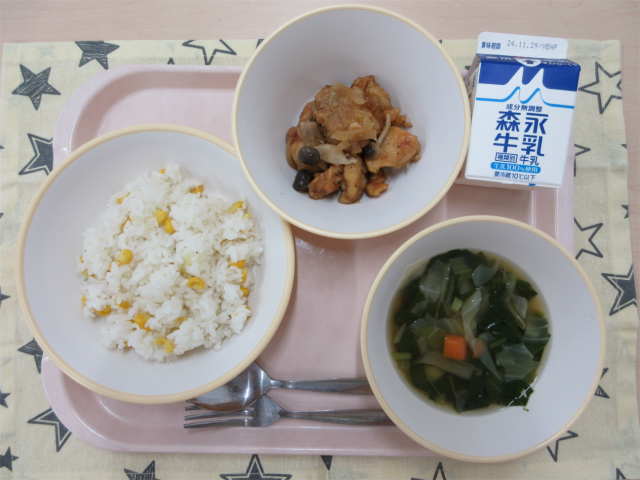 ピンクのトレーに給食が右上から反時計回りで牛乳、鶏肉のガーリック炒め、コーンピラフ、野菜スープと並べられている写真