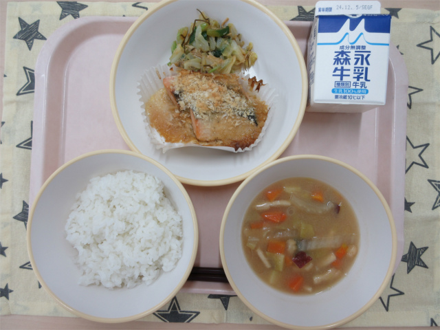 ピンクのトレーに給食が右上から反時計回りで牛乳、ささみとキャベツの昆布和え、鮭のマヨパン粉焼き、ごはん、さつまいもの味噌汁と並べられている写真