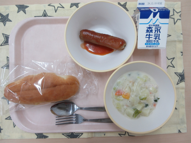 ピンクのトレーに給食が右上から反時計回りで牛乳、ウインナー、コッペパン、ほうれん草のミルクスープと並べられている写真