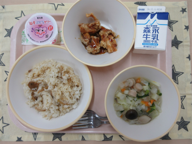 ピンクのトレーに給食が右上から反時計回りで牛乳、鶏肉のかりん揚げ、ぶどうゼリー、ガーリックライス、ポトフと並べられている写真