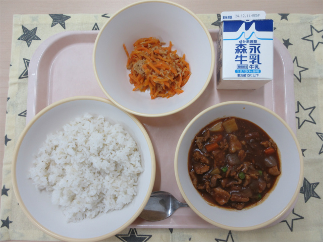 ピンクのトレーに給食が右上から反時計回りで牛乳、にんじんしりしり、麦入りごはん、ハヤシライスのルーと並べられている写真