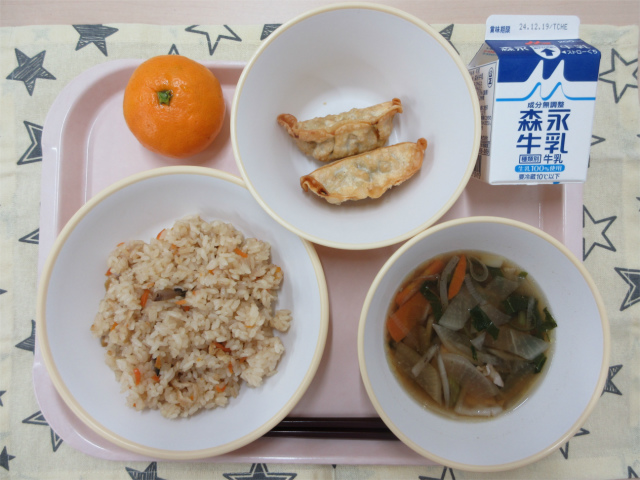 ピンクのトレーに給食が右上から反時計回りで牛乳、揚げ餃子 、みかん、かやくごはん、根菜汁と並べられている写真