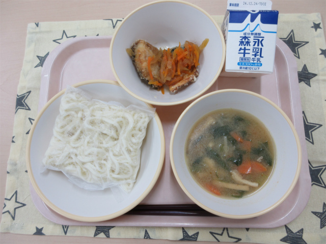 ピンクのトレーに給食が右上から反時計回りで牛乳、さばのゆず南蛮 、ソフト麺、味噌けんちんうどんのスープと並べられている写真