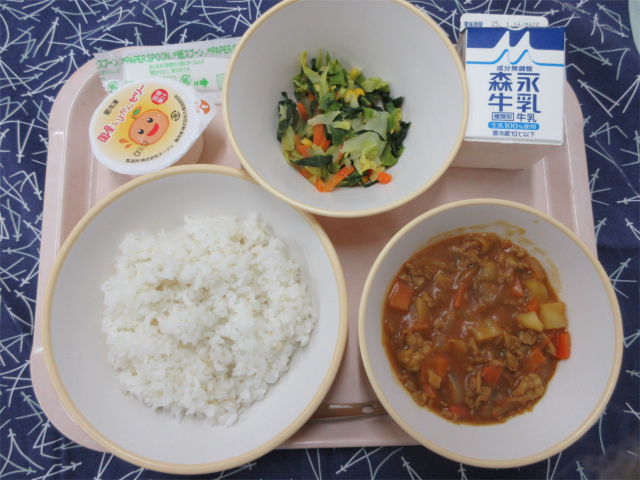 ピンクのトレーに給食が右上から反時計回りで牛乳、野菜ソテー 、いよかんゼリー、もち麦入りごはん、カレーと並べられている写真