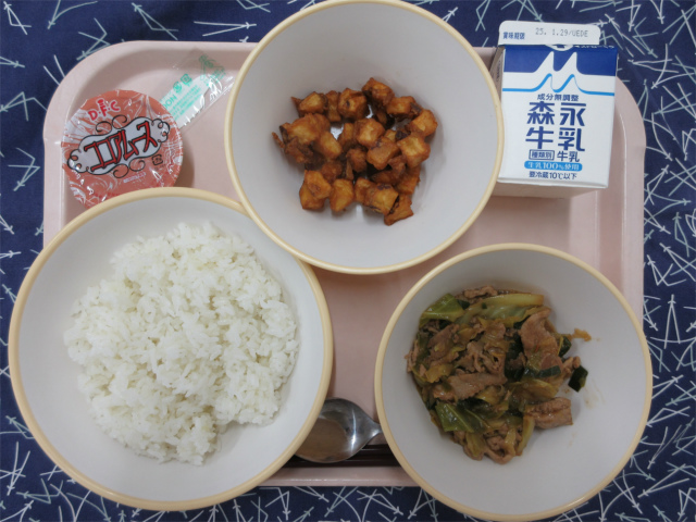 ピンクのトレーに給食が右上から反時計回りで牛乳、さつまいものふわっと揚げ、ココアムース、ごはん、ホイコーロー丼の具と並べられている写真