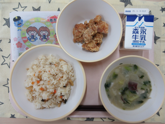 ピンクのトレーに給食が右上から反時計回りで牛乳、鶏肉のから揚げ、手巻きのり、五目寿司、さつま汁と並べられている写真