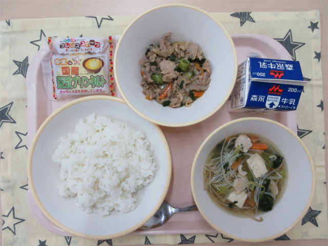 ピンクのトレーに給食が右上から反時計回りで牛乳、葉にんにくと豚肉のピリ辛丼の具、豆乳プリンタルト、ごはん、ビーフンスープと並べられている写真