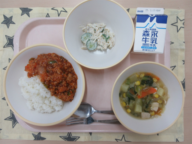 ピンクのトレーに給食が右上から反時計回りで牛乳、ヤーコン入りごまマヨサラダ、タコライス、野菜のスープ煮と並べられている写真