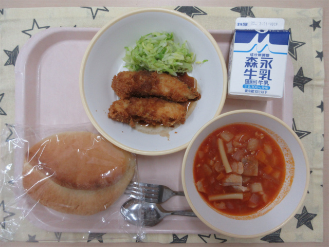 ピンクのトレーに給食が右上から反時計回りで牛乳、白身フライと千切りキャベツ、サンドパン、ミネストローネと並べられている写真