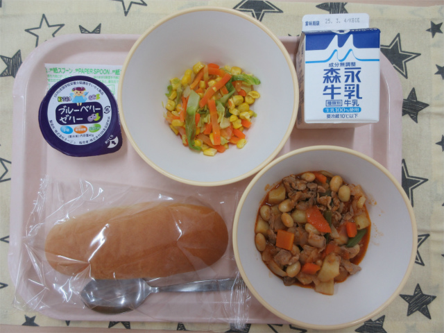 ピンクのトレーに給食が右上から反時計回りで牛乳、コーンソテー、ブルーベリーゼリー、ソフトフランスパン、ポークビーンズと並べられている写真