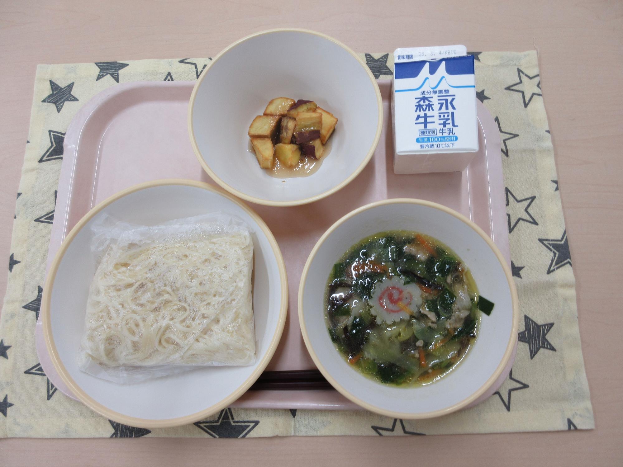 ピンクのトレーに給食が右上から反時計回りで牛乳、キャラメルポテト、麺、五目塩ラーメンと並べられている写真