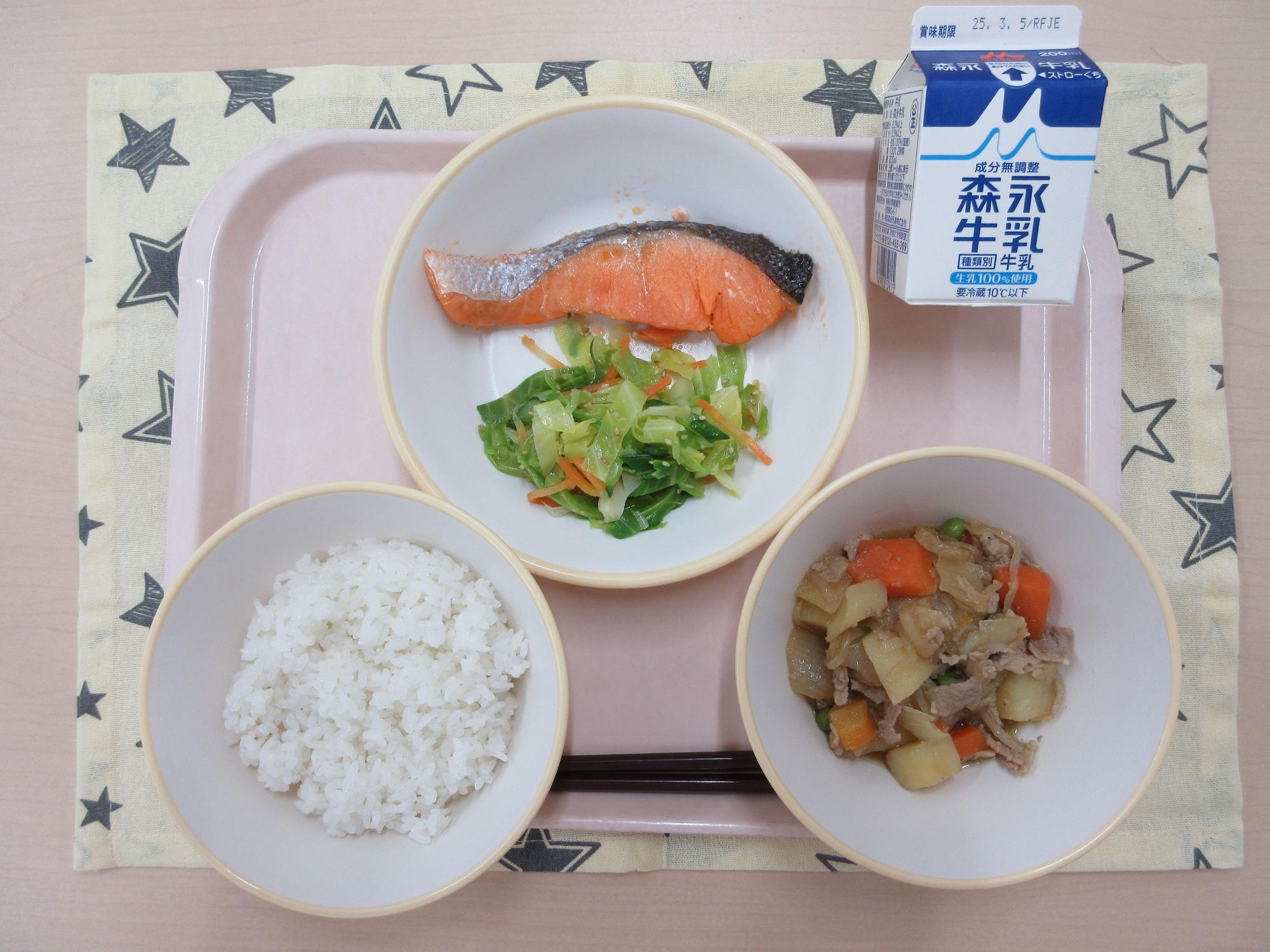 ピンクのトレーに給食が右上から反時計回りで牛乳、鮭の塩焼きとうま塩キャベツ、ごはん、肉じゃがと並べられている写真