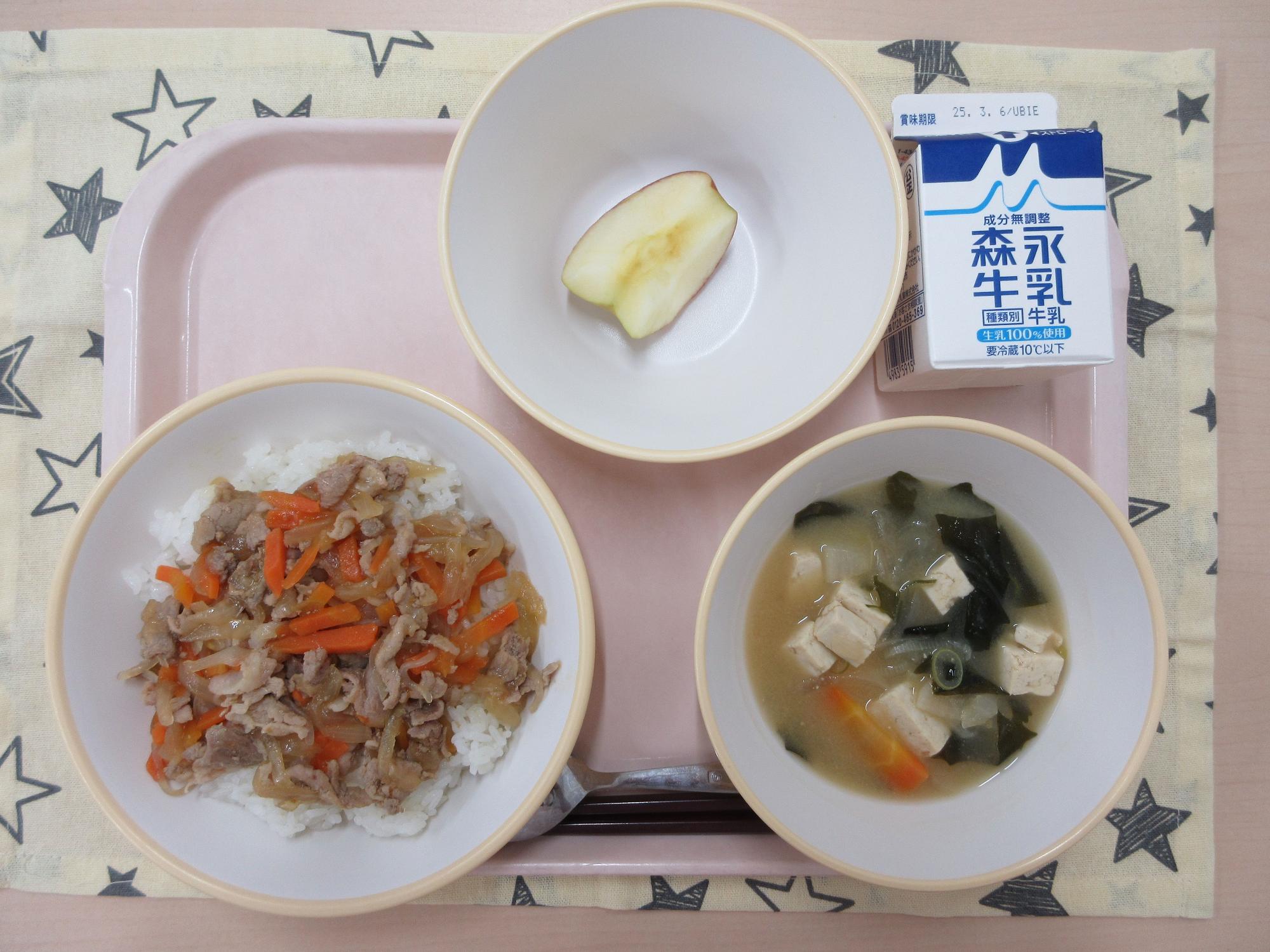 ピンクのトレーに給食が右上から反時計回りで牛乳、りんご（1/6カット）、豚丼、豆腐の味噌汁と並べられている写真