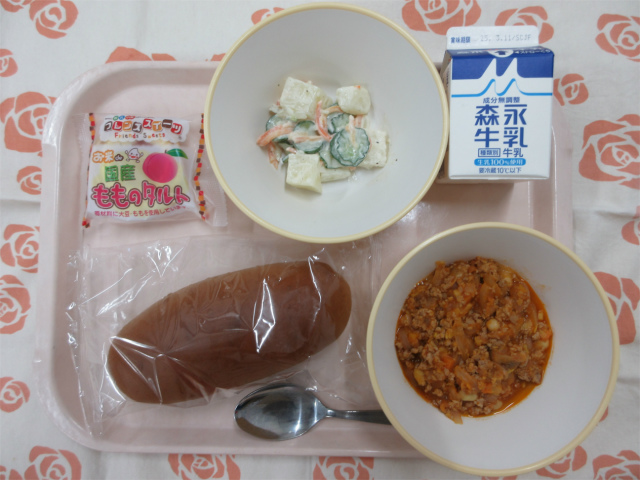 ピンクのトレーに給食が右上から反時計回りで牛乳、ポテトサラダ、ももタルト、黒パン、チリコンカンと並べられている写真