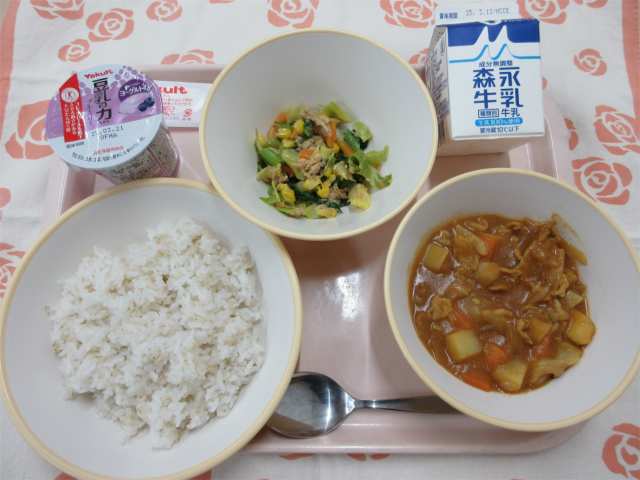 ピンクのトレーに給食が右上から反時計回りで牛乳、野菜のツナ炒め、豆乳ヨーグルト（ブルーベリー）、麦入りごはん、カレーと並べられている写真