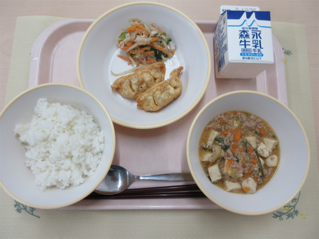 ピンクのトレーに給食が右上から反時計回りで牛乳、揚げ餃子と鶏肉と野菜のナムル、ごはん、麻婆豆腐と並べられている写真
