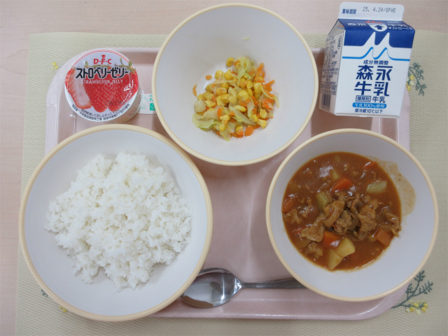 ピンクのトレーに給食が右上から反時計回りで牛乳、コーンソテー、イチゴゼリー、ごはん、カレーと並べられている写真