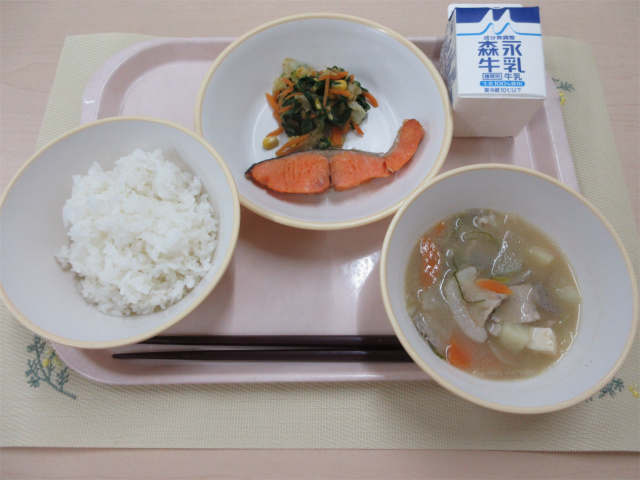 ピンクのトレーに給食が右上から反時計回りで牛乳、鮭の塩焼きとカラフルおひたし、ごはん、豚汁と並べられている写真