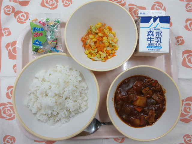 ピンクのトレーに給食が右上から反時計回りで牛乳、コーンソテー、柏餅、もち麦いりごはん、ハヤシライスと並べられている写真