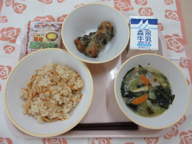 ピンクのトレーに給食が右上から反時計回りで牛乳、ちくわのお茶揚げ、豆乳プリンタルト、たけのこごはん、わかめの味噌汁と並べられている写真