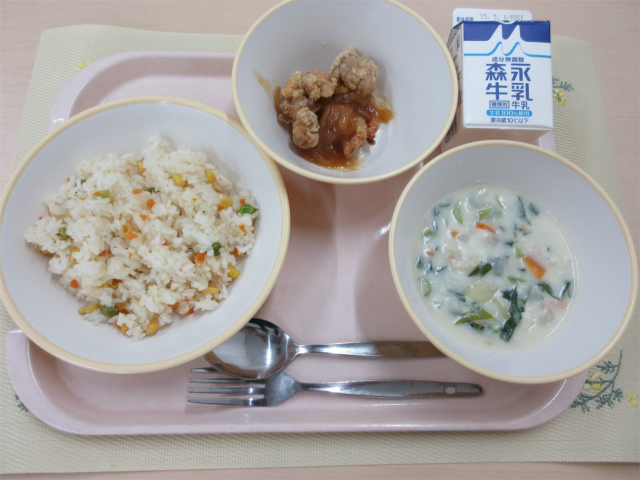 ピンクのトレーに給食が右上から反時計回りで牛乳、鶏肉のバーベキューソース、ベジピラフ、クリームシチューと並べられている写真