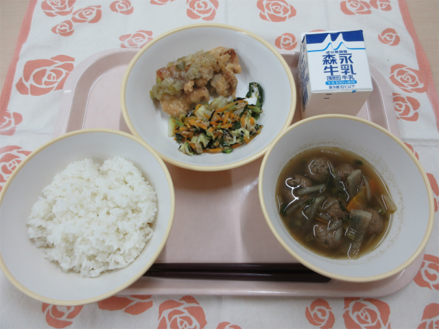 ピンクのトレーに給食が右上から反時計回りで牛乳、鶏肉のねぎ塩だれかけと野菜のツナ炒め、ごはん、根菜汁と並べられている写真