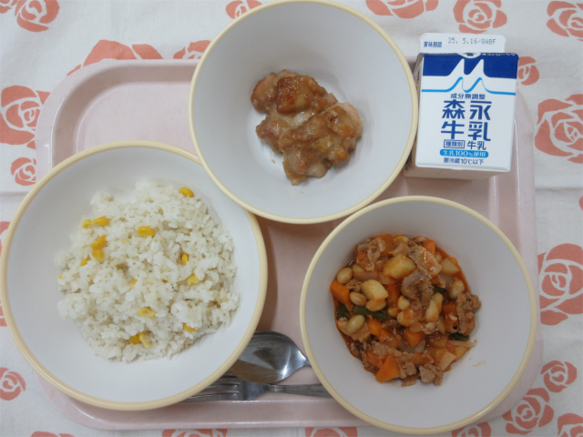 ピンクのトレーに給食が右上から反時計回りで牛乳、モチコチキン、コーンピラフ、ポークビーンズと並べられている写真