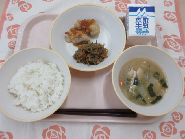 ピンクのトレーに給食が右上から反時計回りで牛乳、鶏肉の生姜焼きときんぴらごぼう、ごはん、じゃがこん汁と並べられている写真