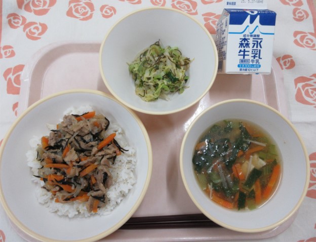 ピンクのトレーに給食が右上から反時計回りで牛乳、野菜の昆布和え、豚丼（麦入りごはん）、あんかけ汁と並べられている写真