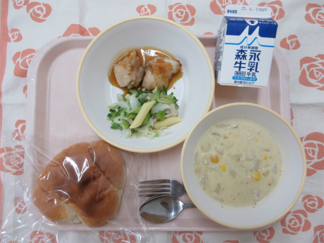 ピンクのトレーに給食が右上から反時計回りで牛乳、テリヤキチキンとグリーンサラダ、ロールパン、コーンシチューと並べられている写真