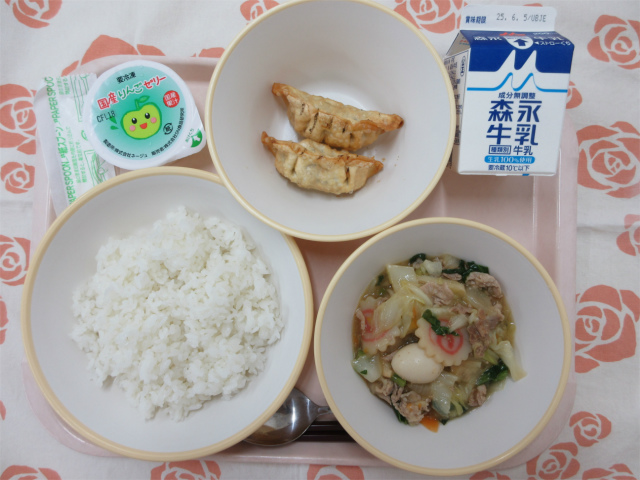 ピンクのトレーに給食が右上から反時計回りで牛乳、揚げ餃子、りんごゼリー、ごはん、中華丼の具と並べられている写真