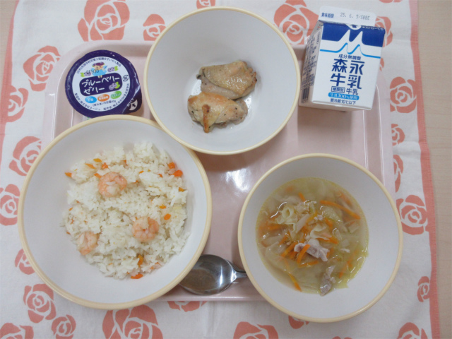 ピンクのトレーに給食が右上から反時計回りで牛乳、鶏肉のハーブ焼き、ブルベリーゼリー、えびピラフ、スコッチブロスと並べられている写真