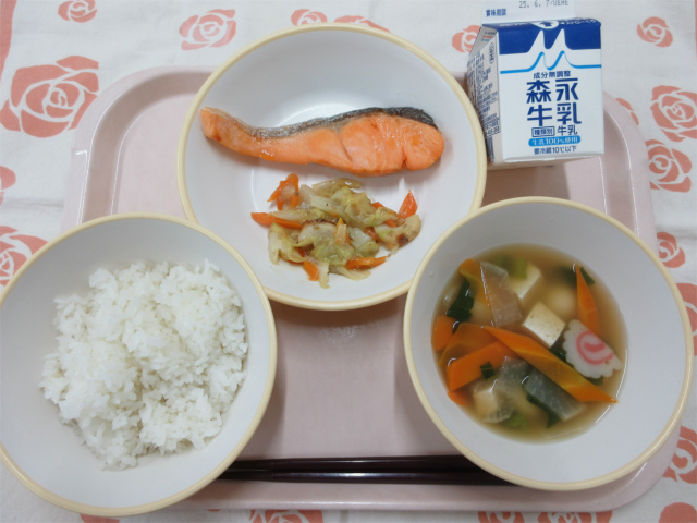 ピンクのトレーに給食が右上から反時計回りで牛乳、鮭の塩焼きと野菜のごま味噌炒め、ごはん、白玉汁と並べられている写真