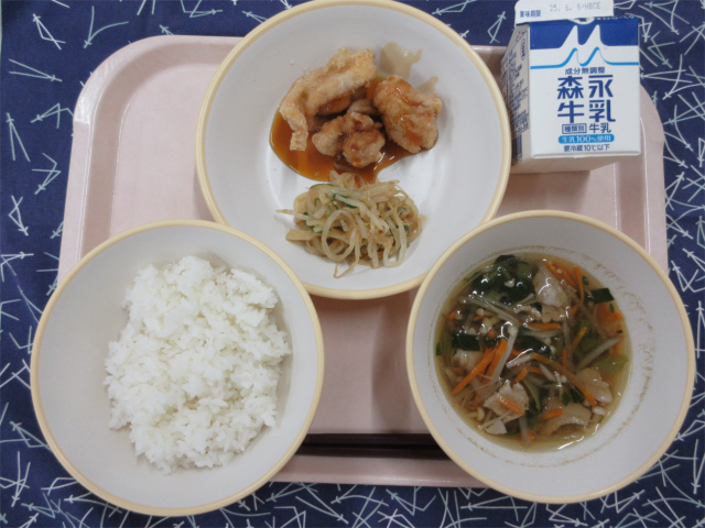 ピンクのトレーに給食が右上から反時計回りで牛乳、鶏肉の甘酢だれとピリ辛もやし、ごはん、沢煮椀と並べられている写真